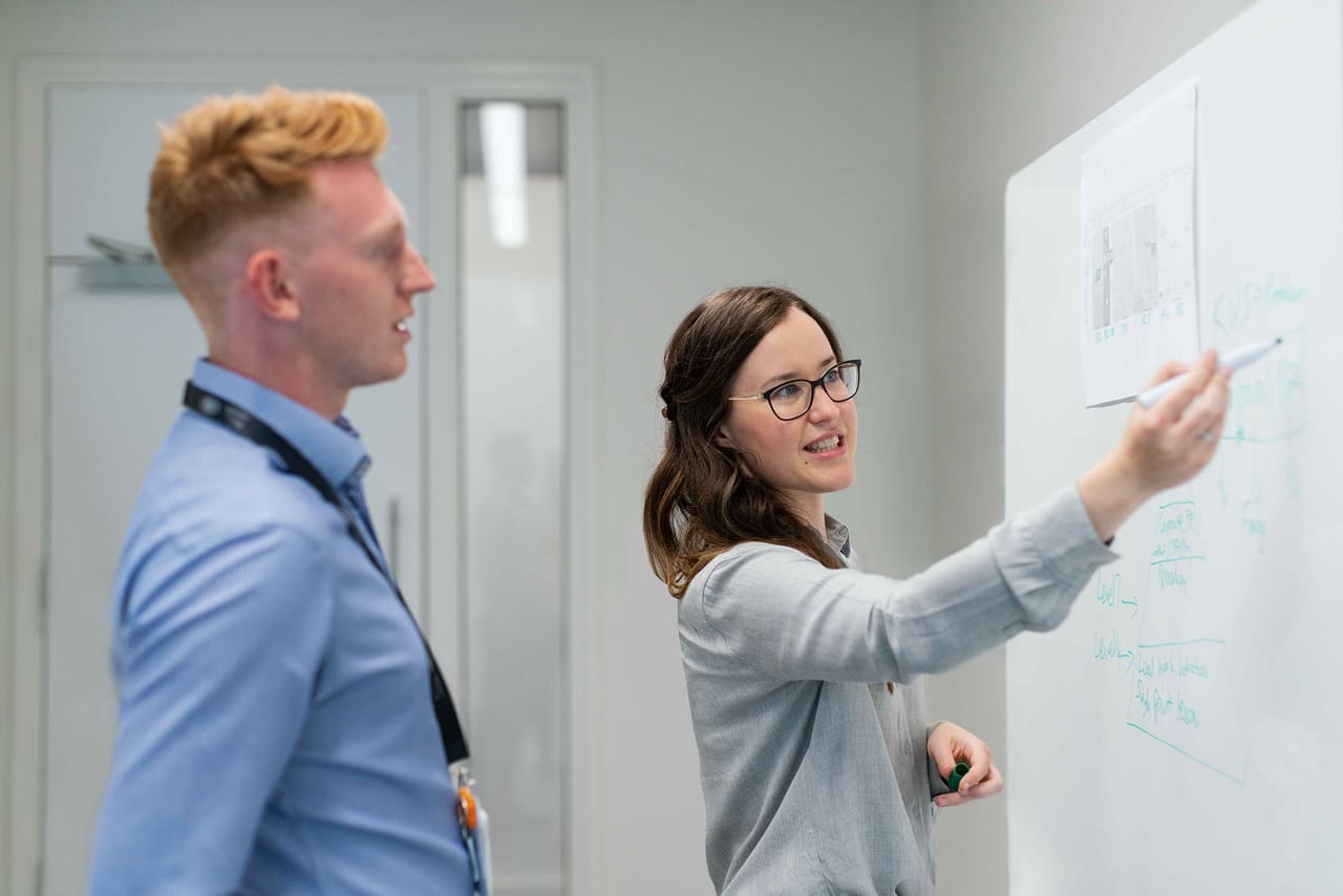 A woman and man are looking at the whiteboard