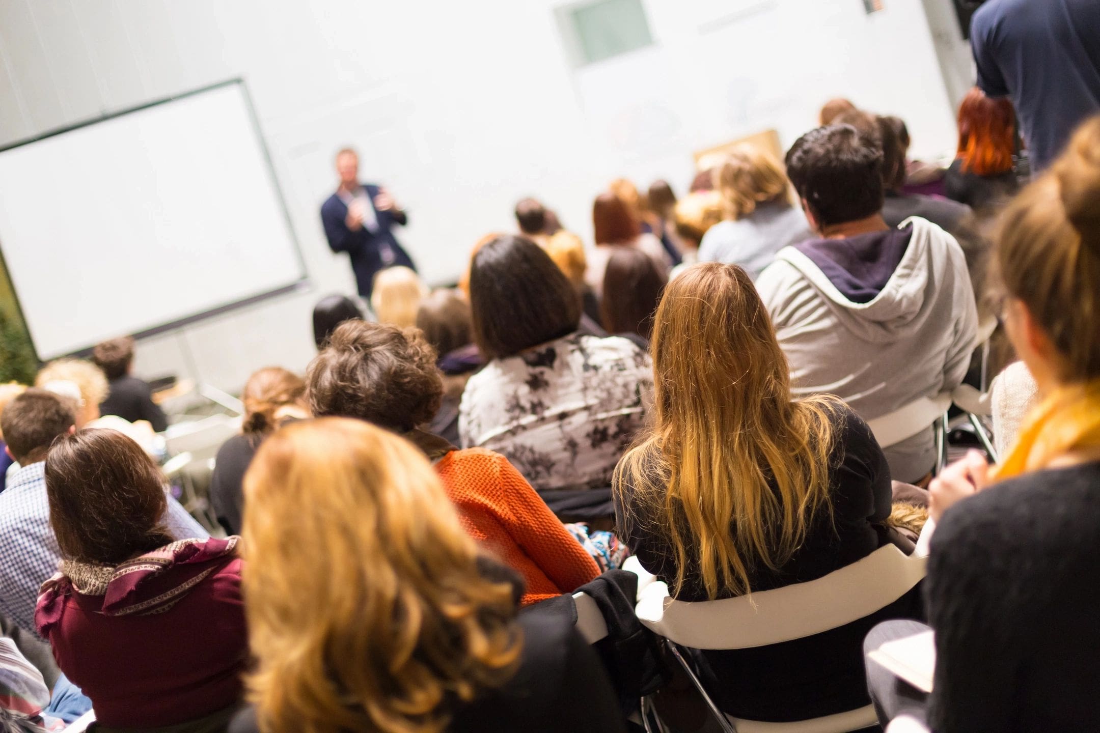 A group of people sitting in front of a projector screen.