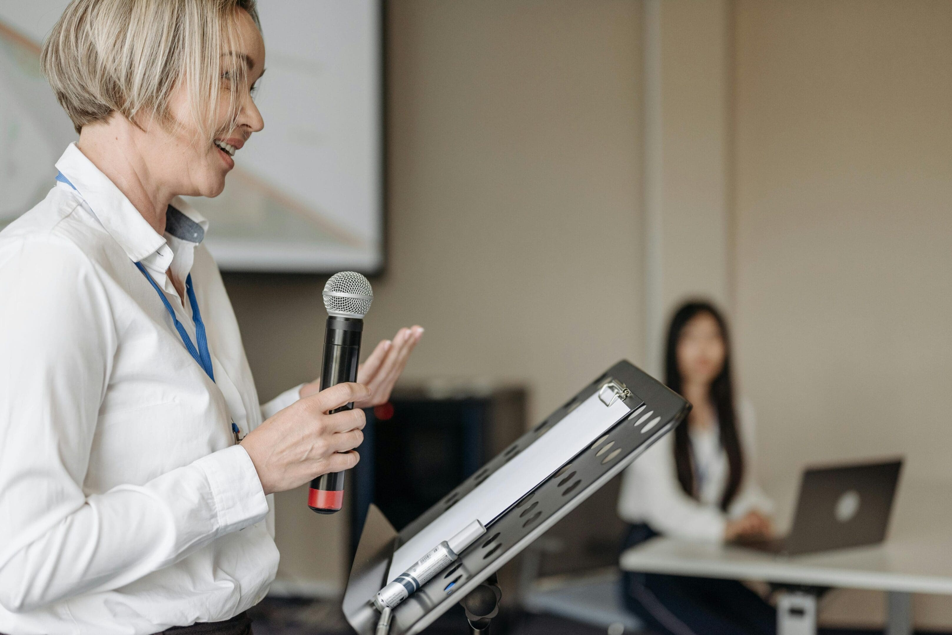 A woman is speaking at an event with microphone.